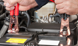 Kiskis Tire Latham NY - A car mechanic uses battery jumper cables to charge a dead battery.